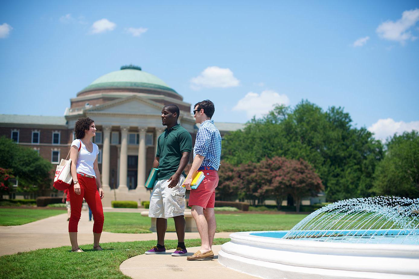 三个学生站在喷泉旁，背景是达拉斯大厅.
