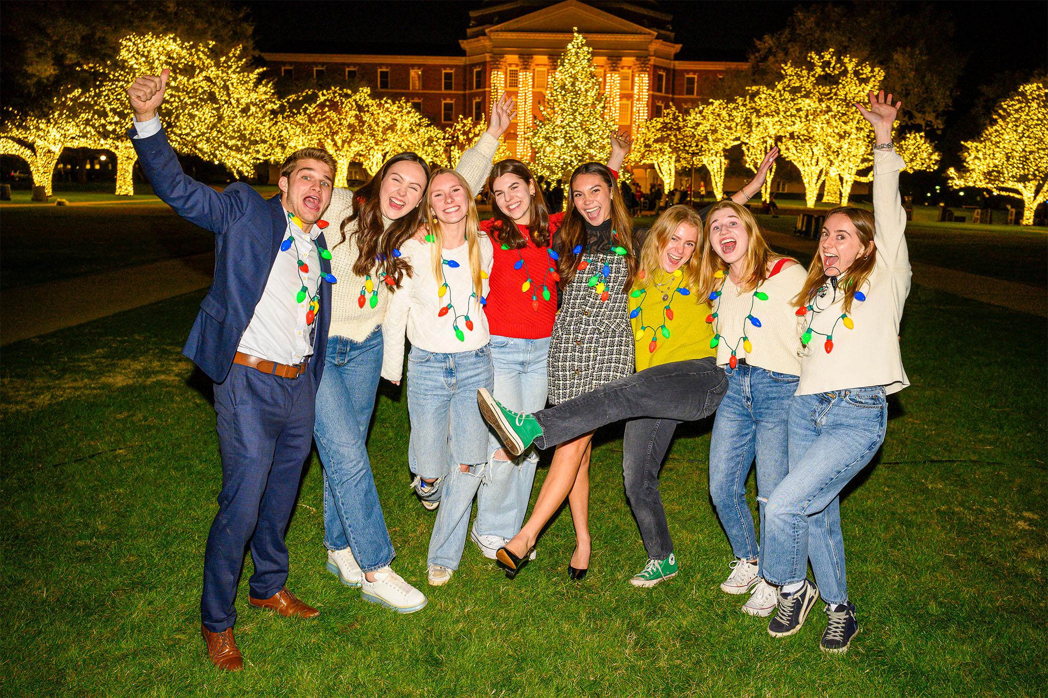 八名学生在达拉斯大厅的草坪上庆祝圣诞树前的庆祝活动